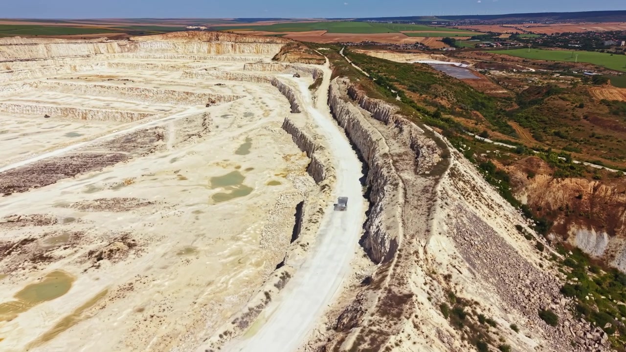 Cava in attività con camion che si muovono lungo strade sterrate, circondata da grandi formazioni rocciose e spazi vuoti