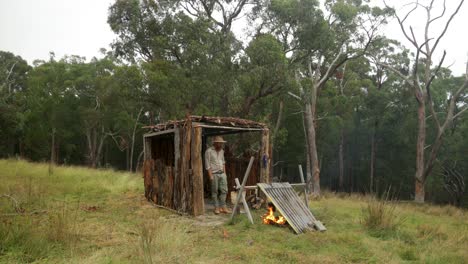 un bushman histórico fumando una pipa de tabaco en su cabaña de corteza en el bosque