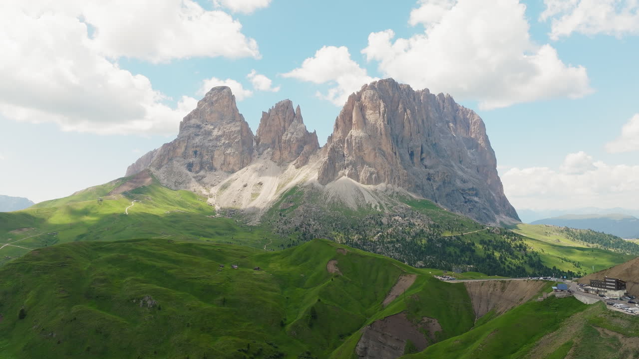 Sassolungo mountain rises behind rolling green pastures and alpine trail in Dolomites