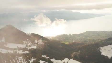 Antena-Extremadamente-Alta-A-Través-De-Las-Nubes-De-Una-Hermosa-Montaña-Cubierta-De-Nieve-Y-Sol-Reflejado-En-El-Lago