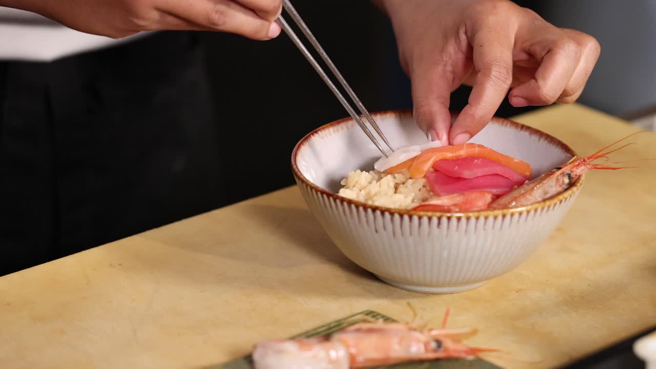 Close-up of chef arranging seafood omakase rice bowl with sashimi under soft studio lighting