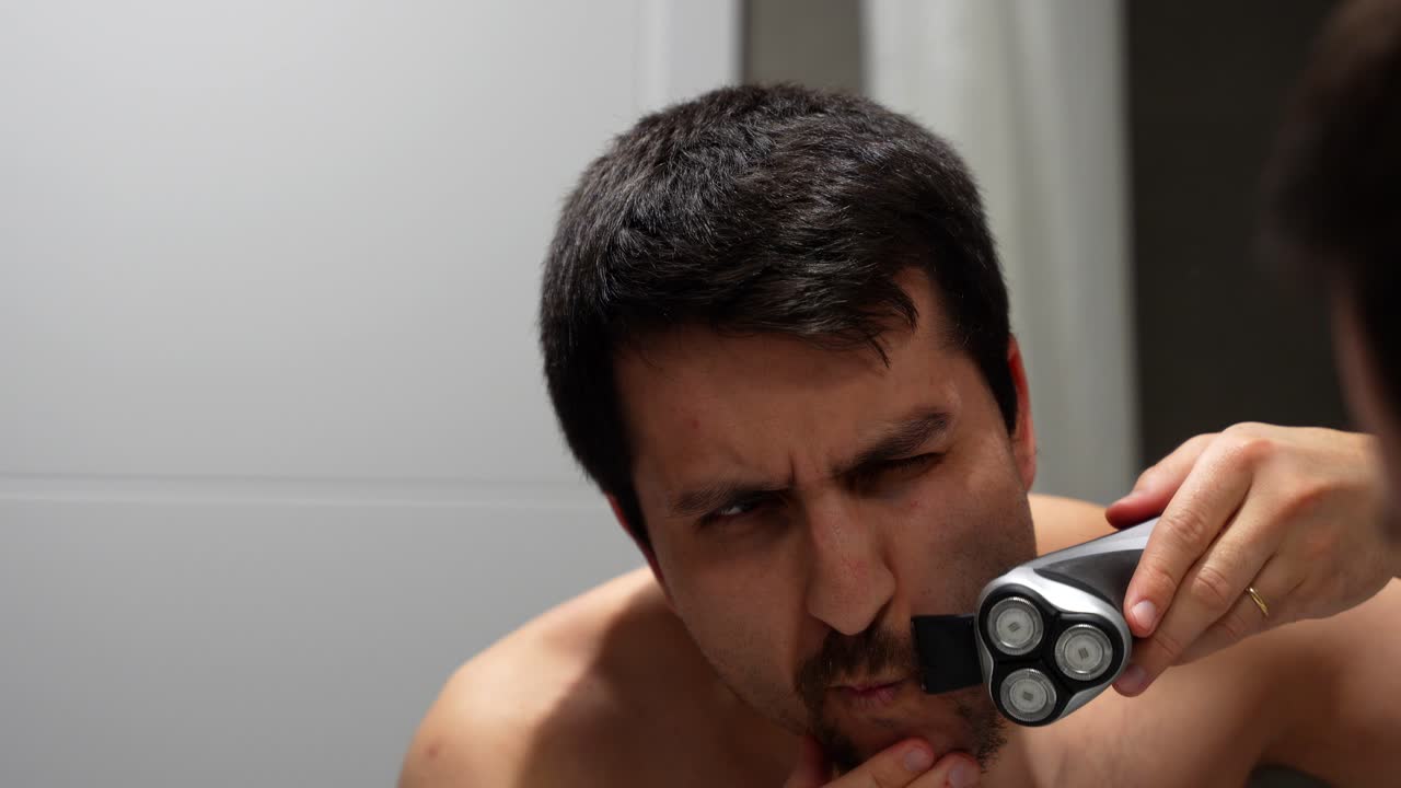 Man shaving goatee in mirror with focus and precision, start of grooming routine
