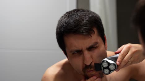 man shaving goatee in mirror with focus and precision, start of grooming routine