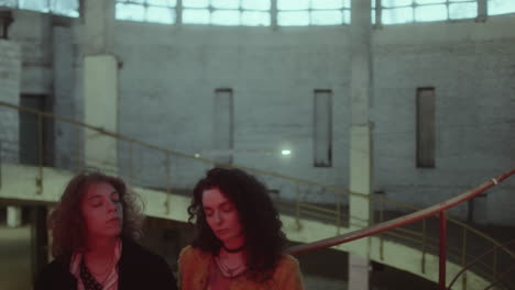 two women contemplating in a moody, industrial building with red light
