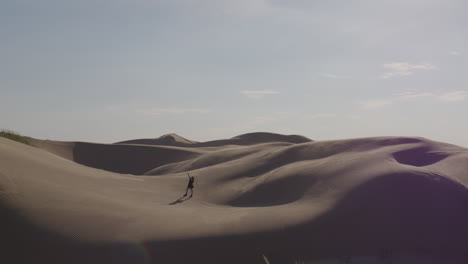 mujer vestida de negro se encuentra entre enormes dunas del desierto con el viento soplando la arena sobre su superficie