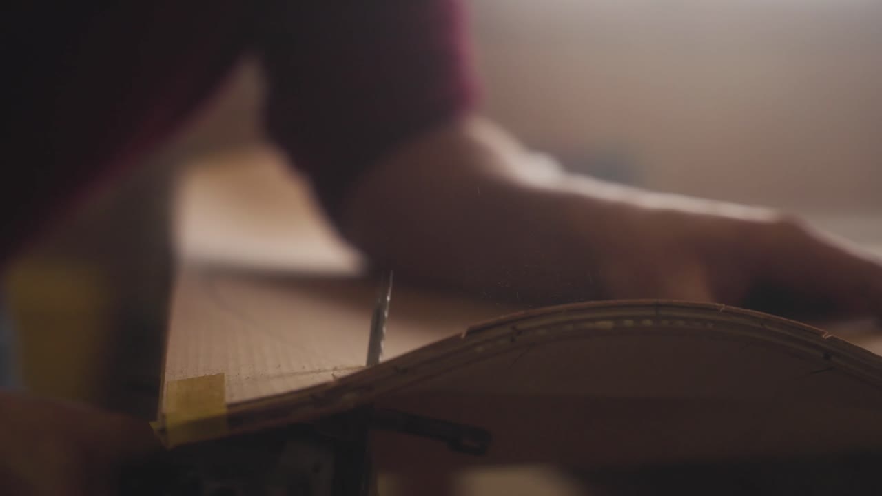 A carpenter saws a skateboard out of a wooden board using a jigsaw