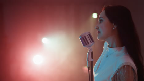 a female singer wearing a white gown stands in front of a vintage microphone, gently moving her hands and body.the side-angle shot captures her graceful and expressive