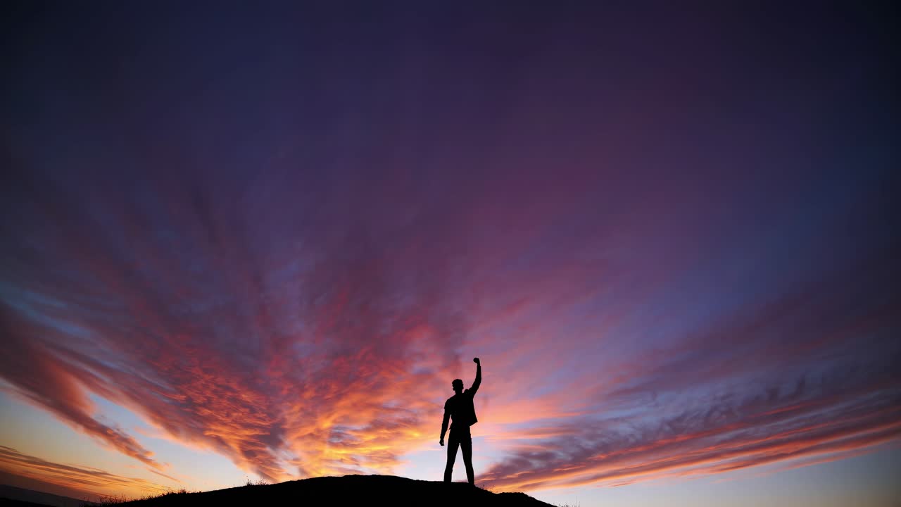 Silhouette di una persona che alza un pugno su una collina al tramonto, ripresa da un'angolazione bassa.
