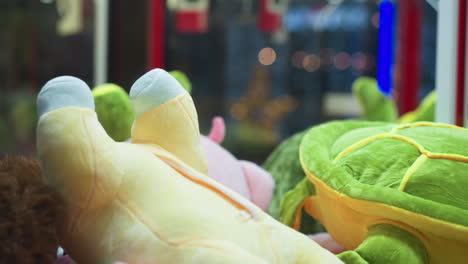 close-up of vibrant plush toys featuring yellow and green stuffed animals in arcade claw machine, with blurred colorful lights in background and subtle reflections