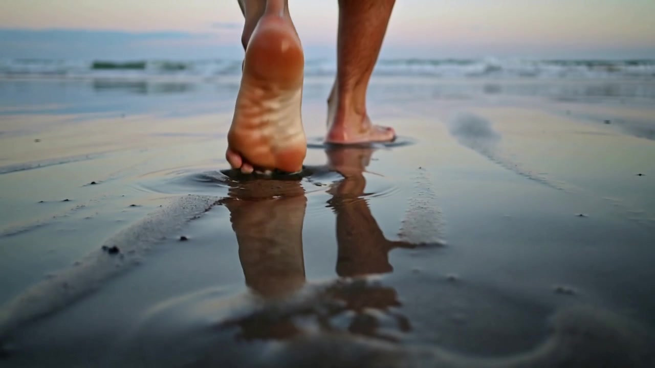 Persona a piedi nudi che preme il tallone, solleva le dita dei piedi e cammina verso il mare sulla sabbia bagnata, lasciando impronte