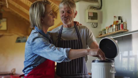 smiling senior caucasian couple wearing aprons, composting vegetable cuttings in kitchen