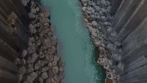 Deep-river-valley-with-rocky-shores-in-Iceland,-aerial-top-down-view