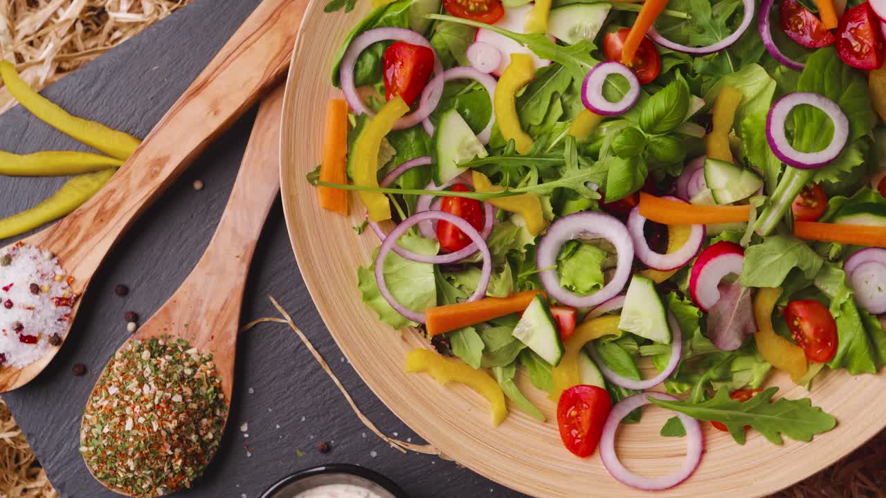 밝은 신선한 농산물, 양파, 토마토, 피망으로 만든 맛있는 샐러드의 버드아이 샷, 슬레이트 접시에 제공, 회전 및 측면 드레싱