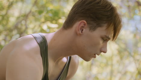 soldier unzips the black jacket and pulls it off while turning head, capturing side view of neck and shoulders, looking around in awe within vibrant forest, surrounded by lush greenery