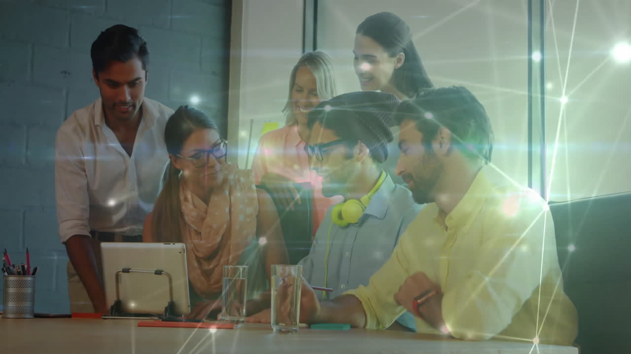 Coworkers leaning around tablet in modern business office glowing nodes showing data flow