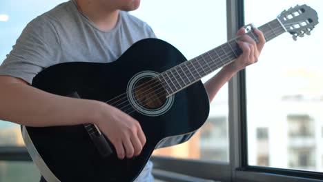 man playing acoustic guitar by the window