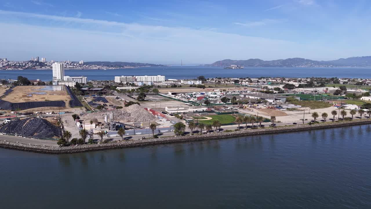 Riprese aeree che sorvolano un grande cantiere a Treasure Island, mostrando lo skyline della città di San Francisco, Alcatraz e il Golden Gate Bridge attraverso la baia in una giornata di sole
