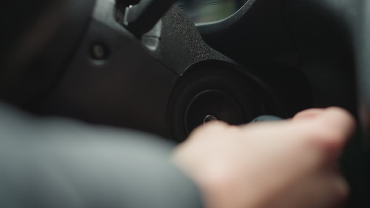 Close up of vehicle owner inserting metal key into ignition starter and turning key inside car cabin focusing on hand movement and dashboard detail while jacket sleeve suggests winter preparation