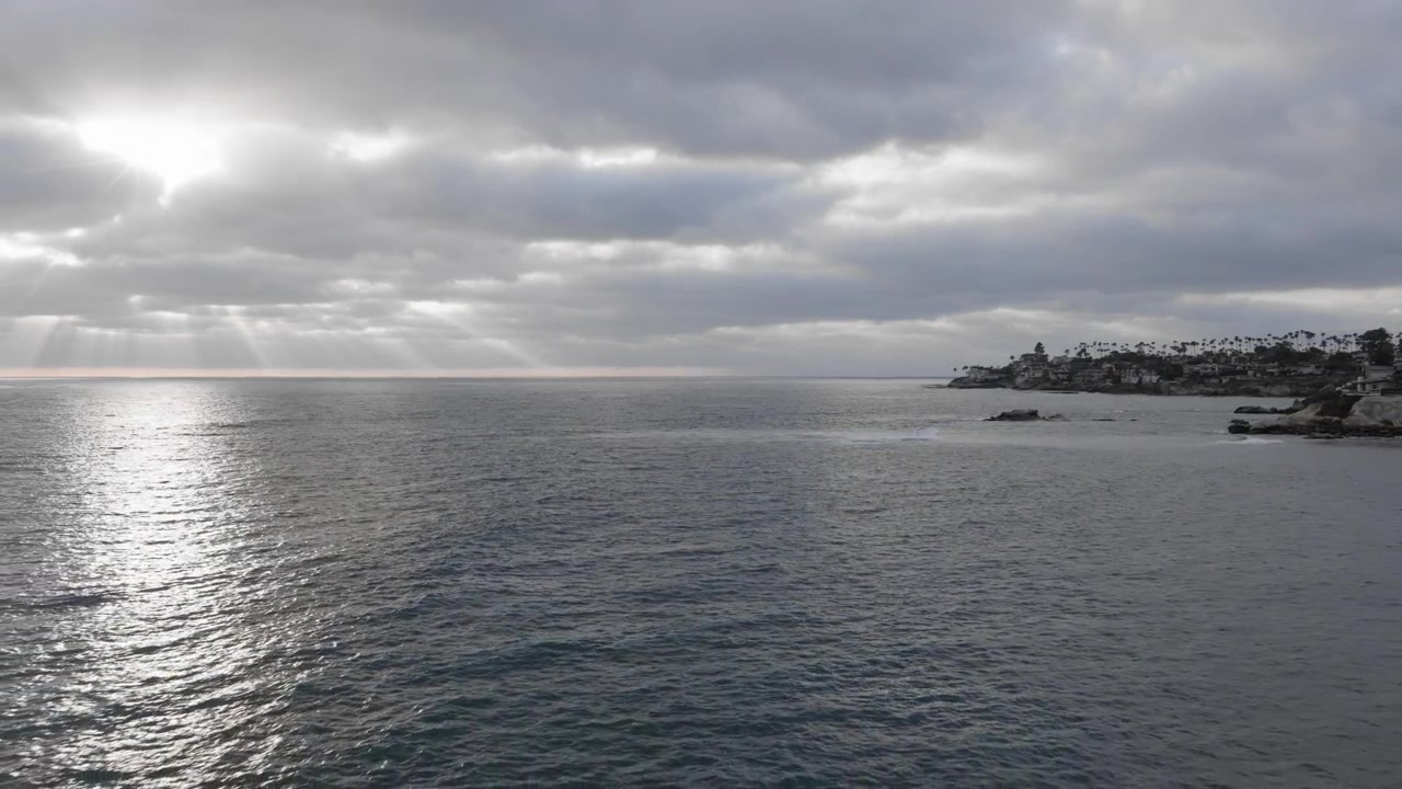 Droneopptak av solstråler som bryter gjennom skyer over La Jolla-kystlinjen - Dolly ut - (UHD 4K)