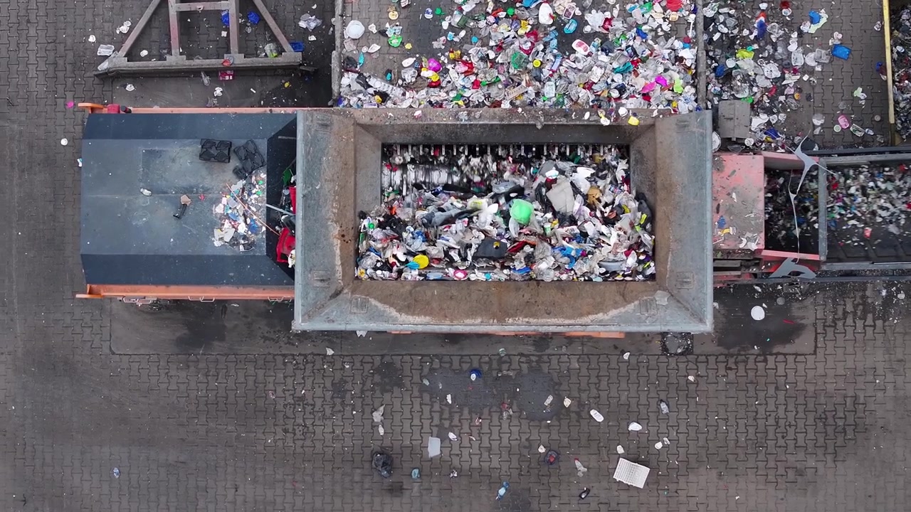 I rifiuti di plastica vengono caricati in un grande contenitore per la selezione e il trattamento. I lavoratori separano i materiali riciclabili dai rifiuti non riciclabili. L'impianto opera in un'area industriale