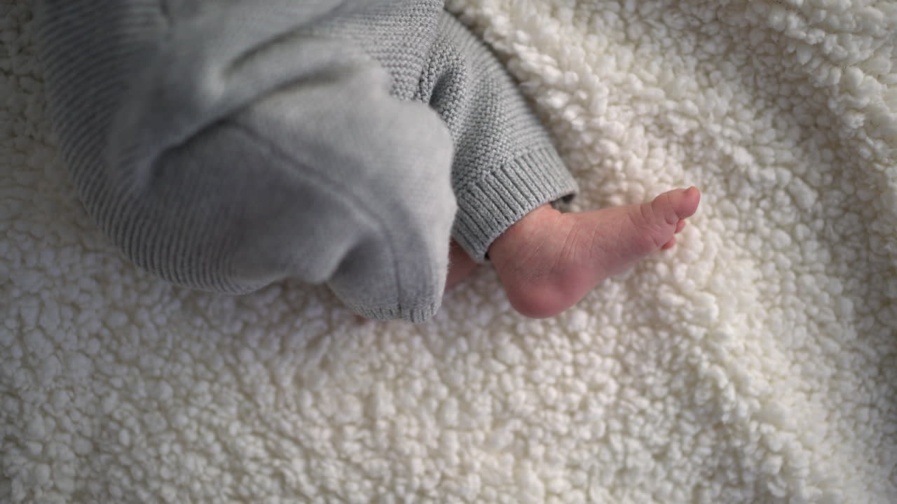 Baby foot in gray knit pants on white blanket
