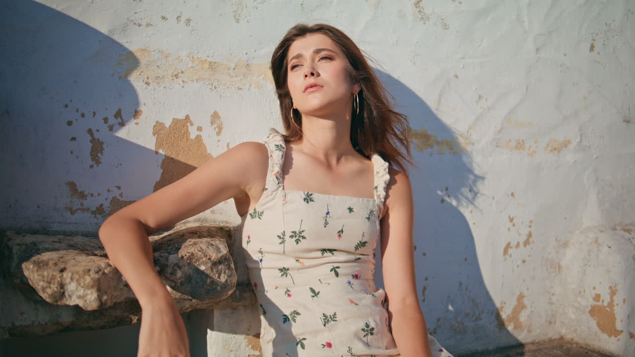 mujer cansada mirando hacia el sol sentada en el banco de la ciudad. mujer tocando el cabello ventoso