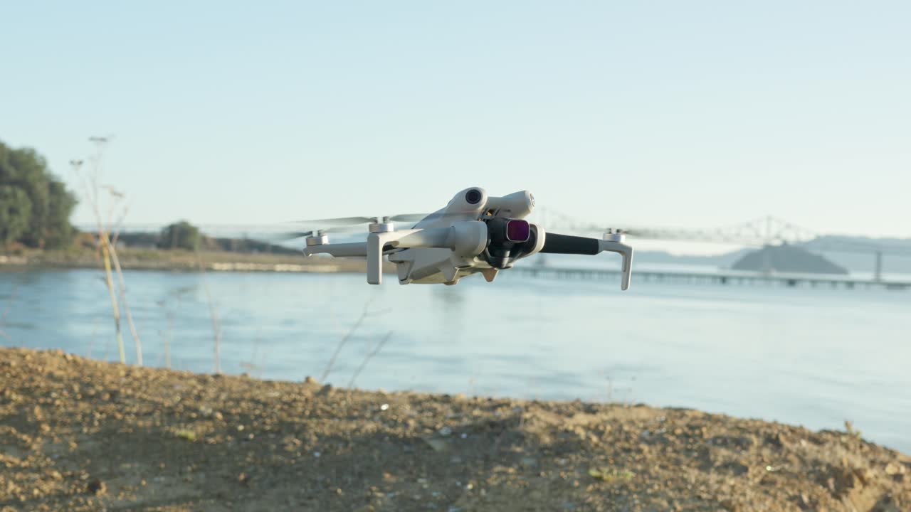 The small drone hovers steadily over a beach, with the Richmond–San Rafael Bridge framing the scene in the distance beneath soft daylight