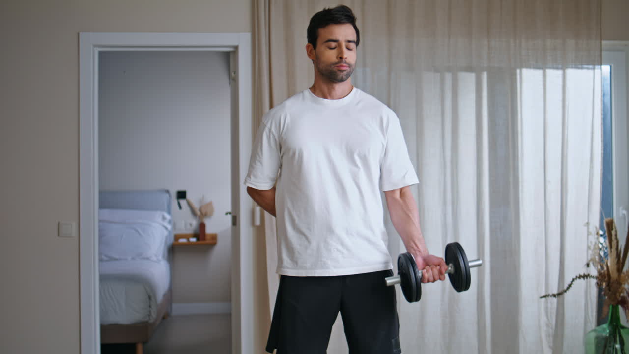 Strong man lifting dumbbell at strength training home. Determined sportsman