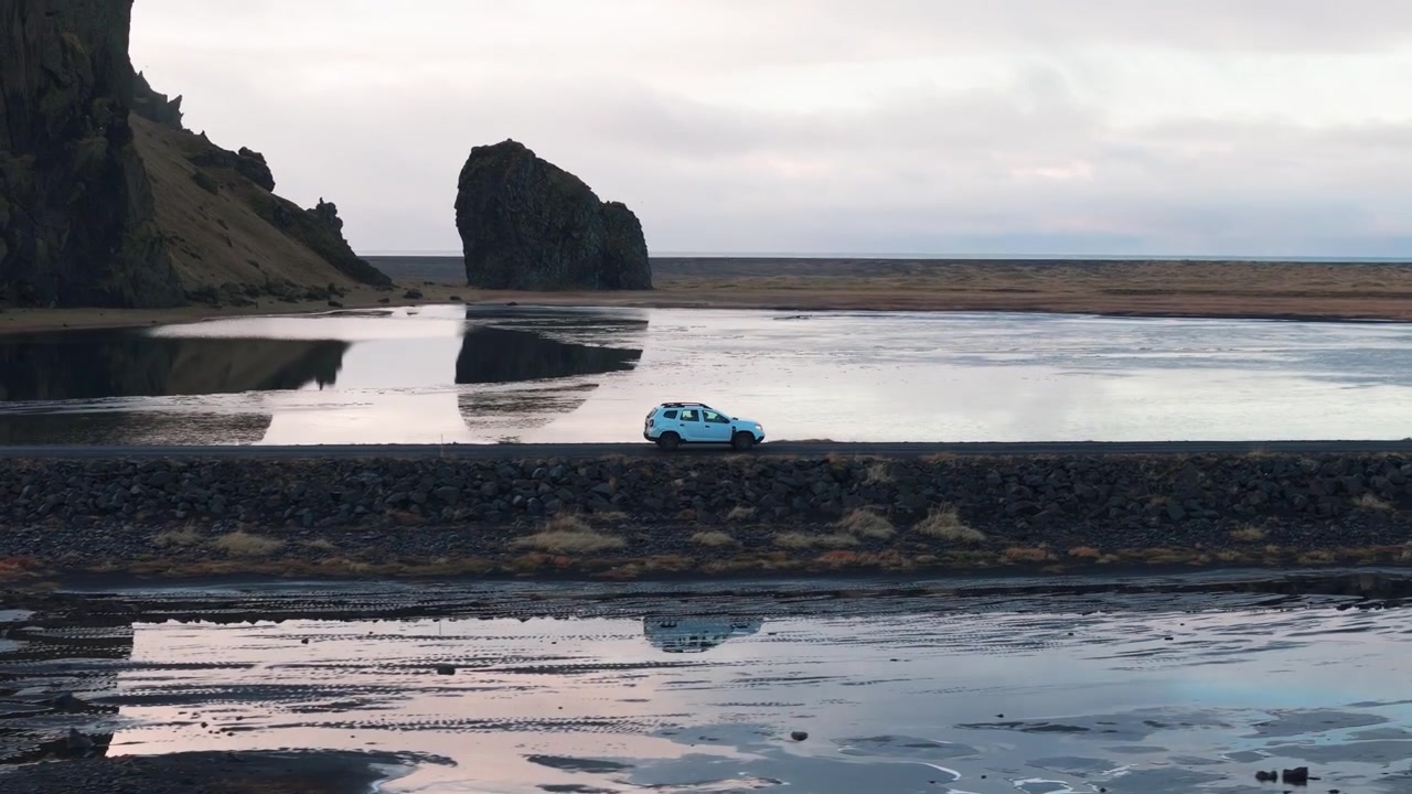 Bil kører langs naturskøn sort sandstrand med unikt klippelandskab på Island.