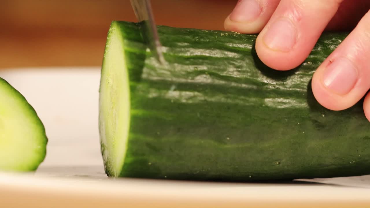 Forward shot of a person slicing a cucumber with a knife