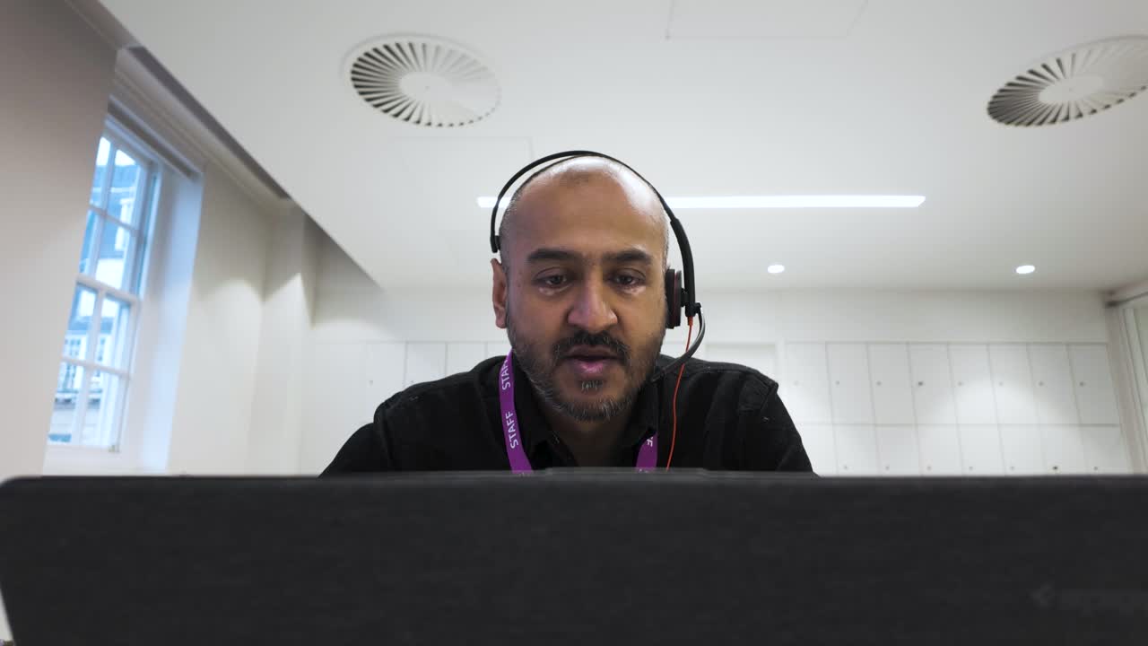 Man in headset engaged in a video call, indoors, natural light from windows