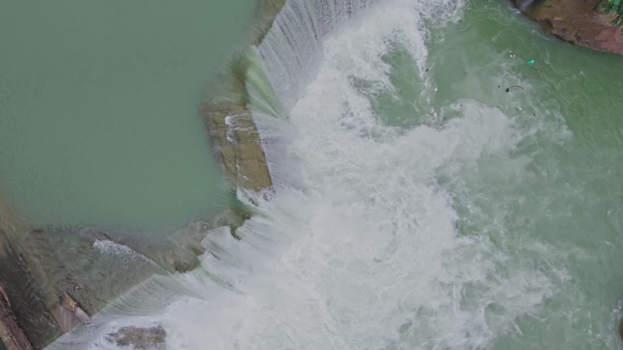 Aerial drone view of a beautiful waterfall merging into a flowing river, capturing the natural beauty of water movement, rocky terrain, and pristine landscape