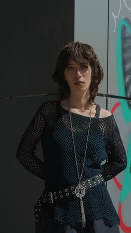 retrato vertical de moda al aire libre de una mujer joven de estilo alternativo apoyándose en una pared cubierta de graffiti en la calle de la ciudad de londres, reino unido, en tiempo real.