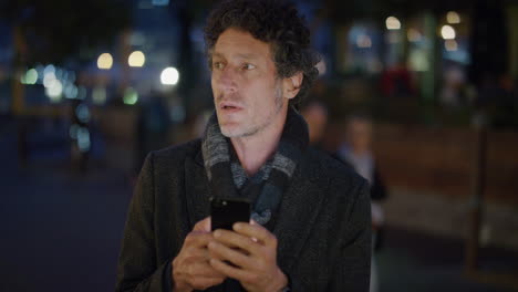 retrato de un atractivo turista maduro que usa un teléfono inteligente esperando en la calle enviando mensajes de texto navegando por internet buscando direcciones en el teléfono móvil en la ciudad por la noche en cámara lenta