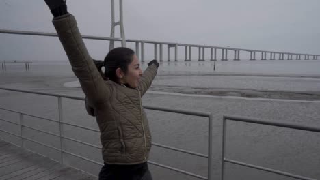 happy brunette woman with raised hands posing at seaside