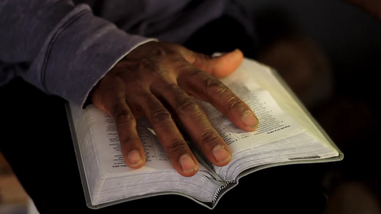 rezando a dios con la mano en la biblia con fondo gris almacen de video