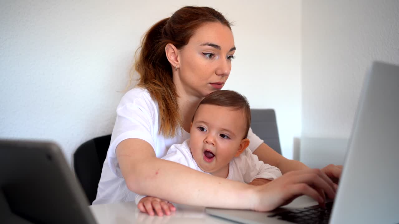Mother using laptop and baby watching cartoons on tablet