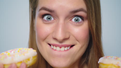 closeup joyful woman eating donut with big appetite on grey background.