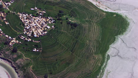 vista aérea rotacional sobre el pueblo rodeado por un río seco, montañas y granjas y árboles verdes