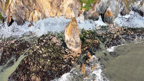 ireland epic drone view of shore and sea stack with incoming waves at copper coast waterford ireland at low tide