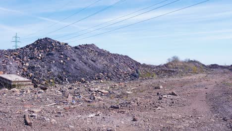 Exterior-view-of-abandoned-Soviet-heavy-metallurgy-melting-factory-Liepajas-Metalurgs-territory,-piles-of-debris-and-junk,-distant-electrical-powerlines,-sunny-day,-wide-shot