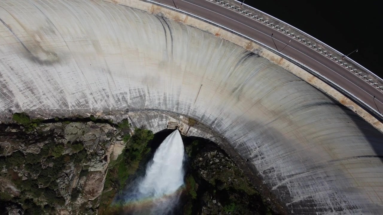 4K aerial drone video advancing and tilting down to capture the massive concave concrete wall of the Almendra Dam in Salamanca, Spain. The impressive shot highlights the immense engineering structure