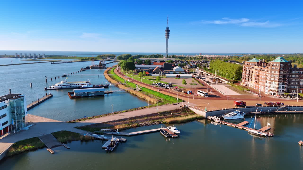 Marina with several berths and boats near them. Approaching the tower for television broadcasting in the scenery of Lelystad, the Netherlands.
