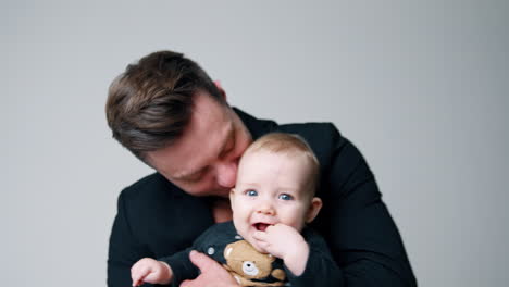 happy caucasian daddy in black jacket holding a cute little baby. lovely child chewing the hand and smiling. white backdrop.