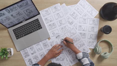 close up top view of asian male artist drawing storyboard for the film on the table with a laptop and headphones in the studio