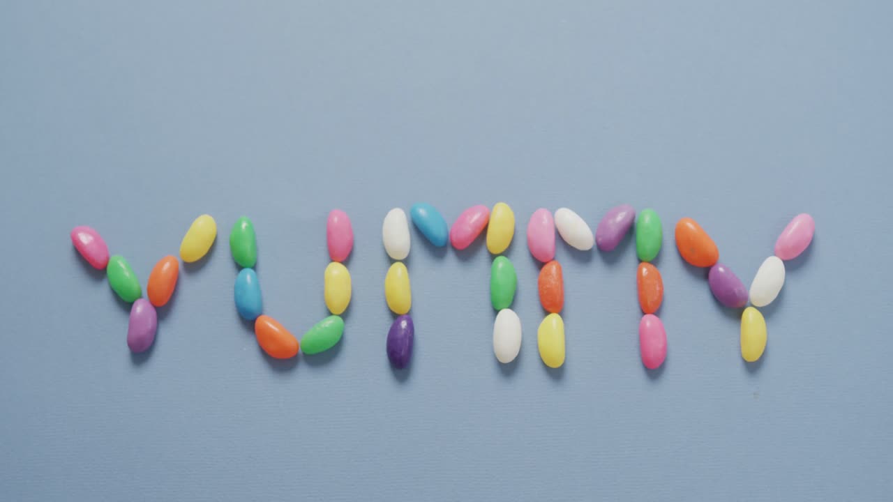 파란색 배경 위에 다채로운 과자 형태의 맛있는 텍스트의 오버헤드 뷰 비디오