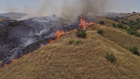 intense wildfire engulfs hillside landscape, creating a dramatic scene of fire and smoke as it spreads across dry grasslands and forested areas