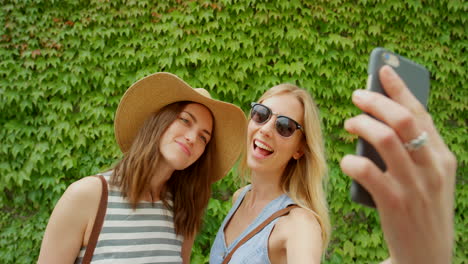 two women taking a selfie in front of an ivy-covered wall