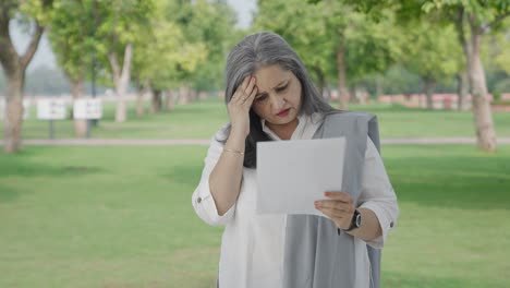 una anciana india estresada leyendo informes en el parque.