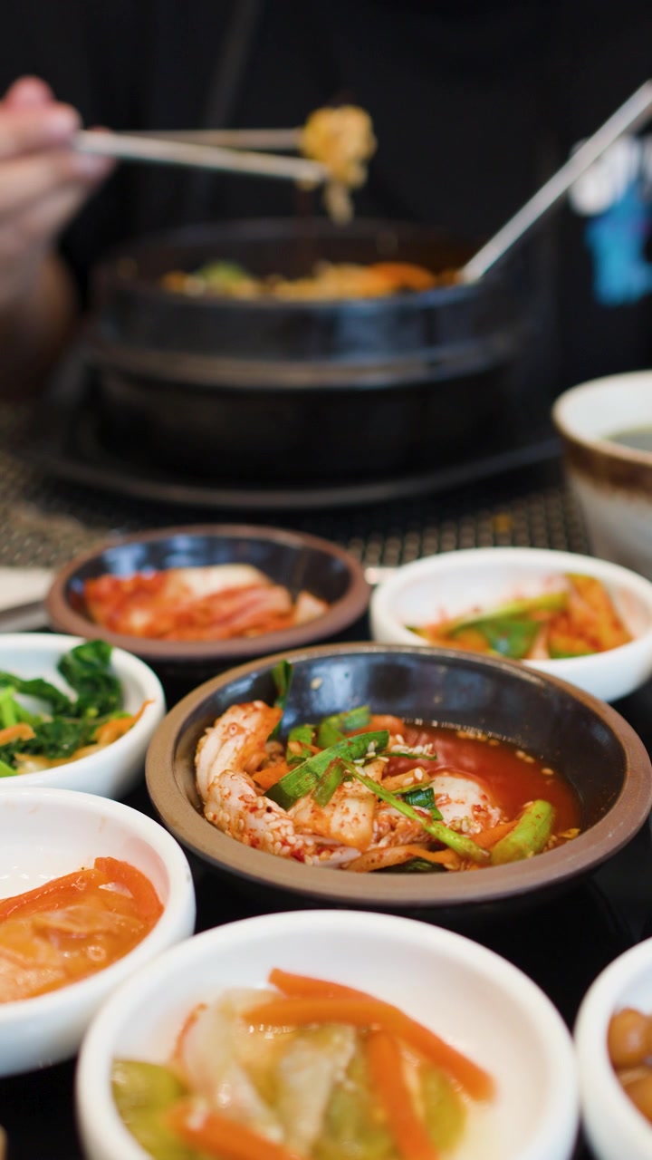 Close-up seorang pengunjung restoran menggunakan sumpit logam untuk makan berbagai hidangan pendamping Korea
